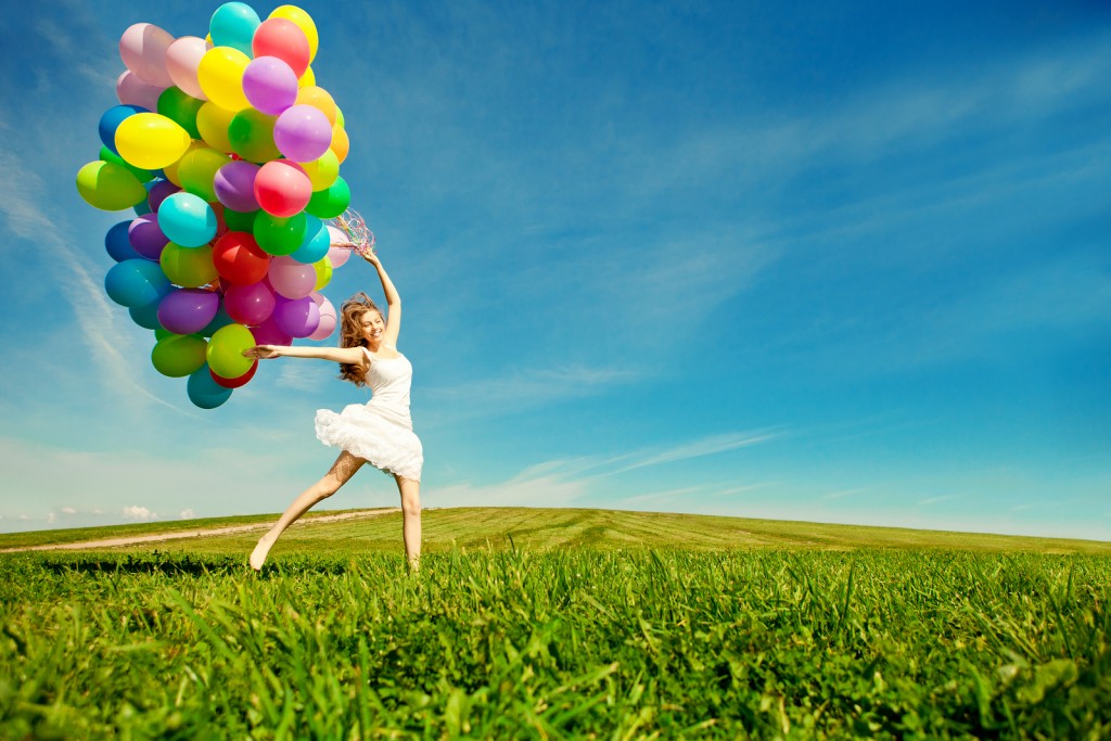 Happy birthday woman against the sky with rainbow-colored air balloons in hands. sunny and positive energy of nature. Young beautiful girl on the grass in the park.